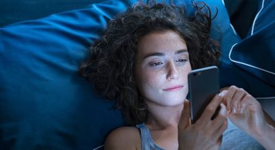 Woman in bed looking at a smartphone to put dryer on using app control.