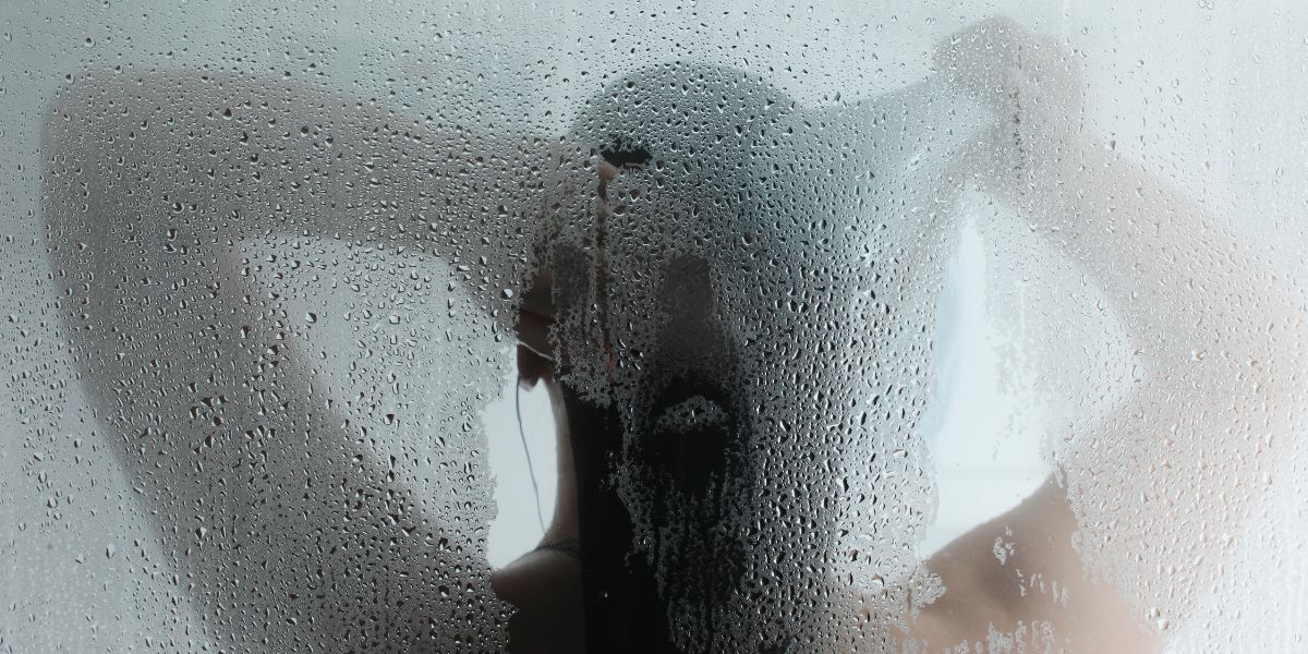 A steamed-up shower screen with the silhouette of a woman washing her hair with a handheld shower head