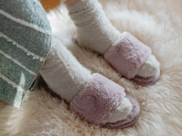 Feet in woollen socks and fluffy slippers on a fluffy white rug.