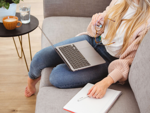 A woman works from warm comfortable home sitting on sofa with a laptop.